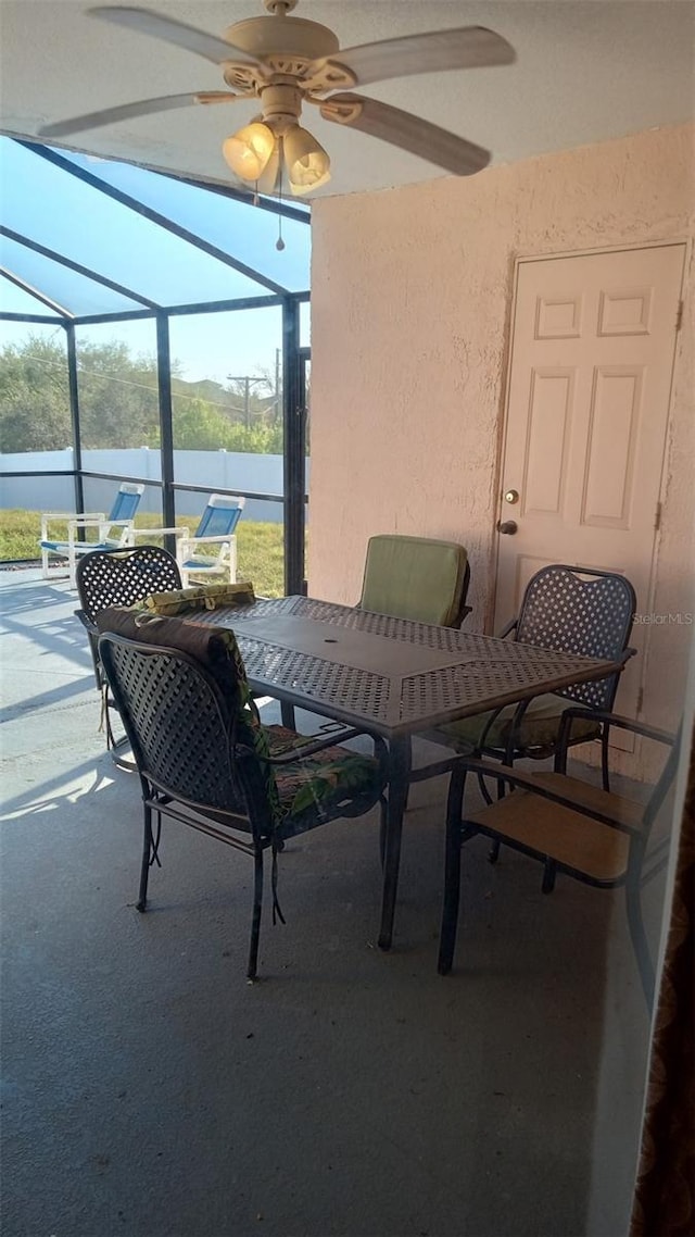view of patio featuring a ceiling fan, glass enclosure, and outdoor dining area