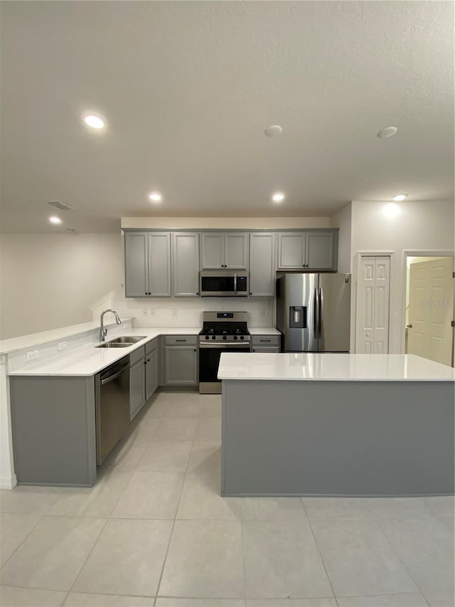 kitchen with recessed lighting, a sink, gray cabinetry, light countertops, and appliances with stainless steel finishes