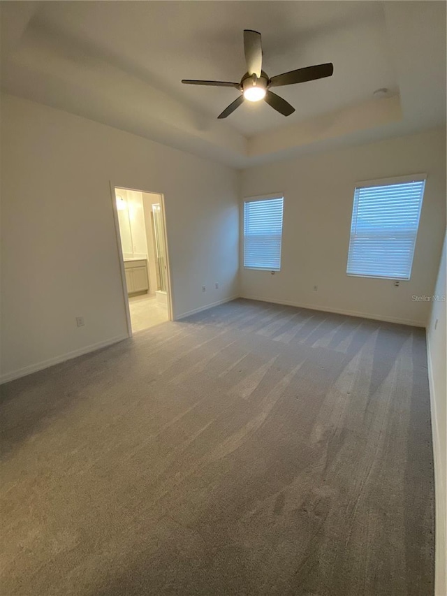 unfurnished room featuring carpet flooring, baseboards, a raised ceiling, and a ceiling fan