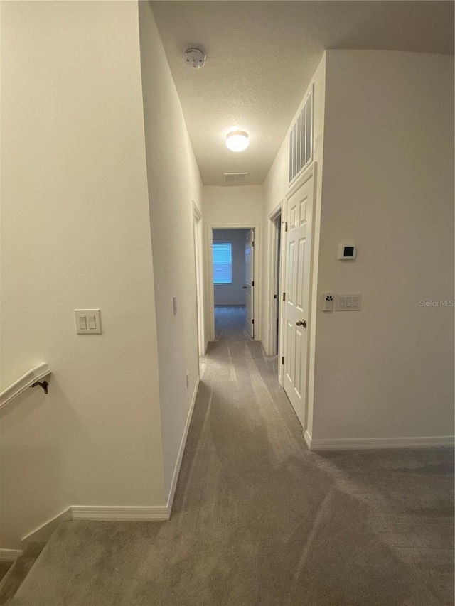 hall featuring baseboards, visible vents, carpet floors, and a textured ceiling