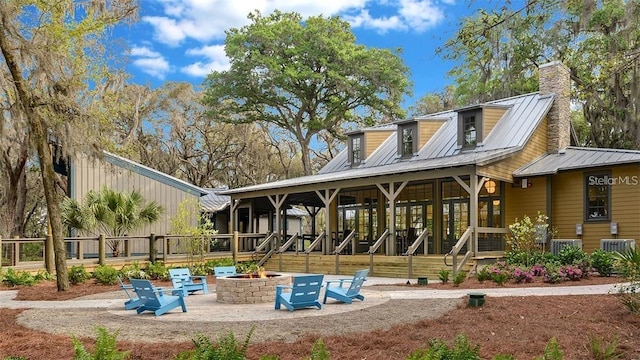 back of house featuring an outdoor fire pit, a standing seam roof, a chimney, metal roof, and a patio