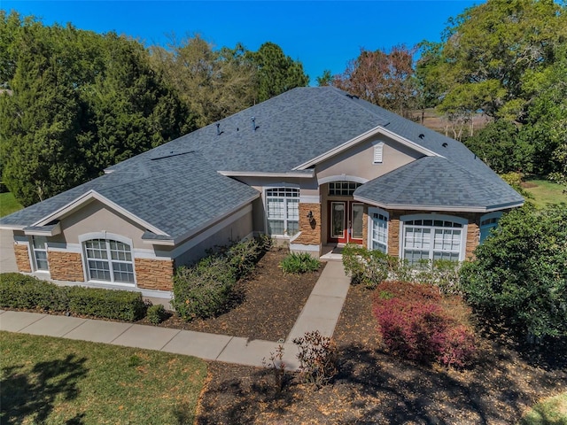 single story home featuring stone siding, stucco siding, and roof with shingles