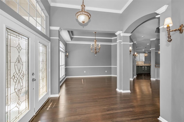 foyer with a chandelier, crown molding, ornate columns, and wood finished floors