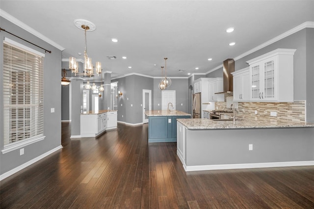 kitchen with a sink, stainless steel appliances, a large island, wall chimney range hood, and a notable chandelier