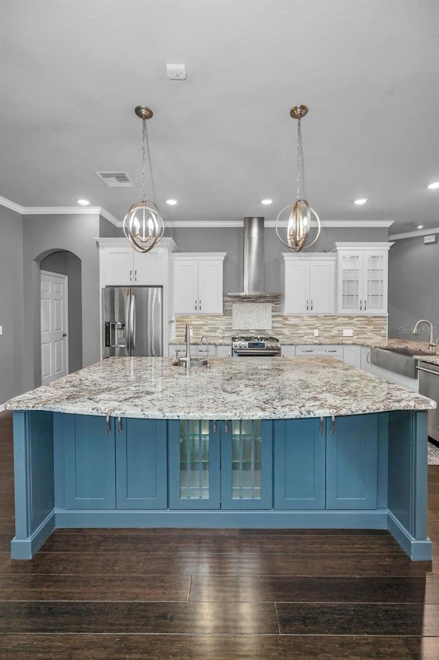 kitchen with blue cabinetry, stainless steel appliances, a large island, and wall chimney range hood