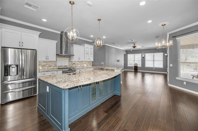 kitchen with stainless steel appliances, white cabinets, crown molding, wall chimney exhaust hood, and ceiling fan with notable chandelier