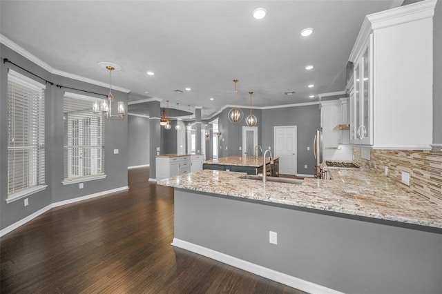 kitchen featuring a peninsula, an island with sink, a sink, dark wood-type flooring, and crown molding