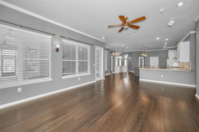 unfurnished living room with ornamental molding, ceiling fan with notable chandelier, dark wood finished floors, recessed lighting, and baseboards