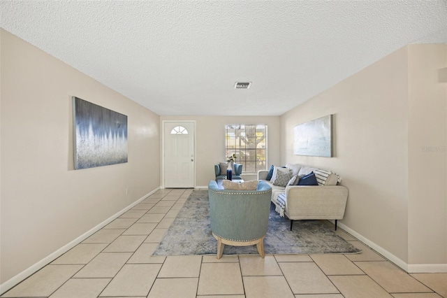 living area featuring light tile patterned floors, visible vents, a textured ceiling, and baseboards