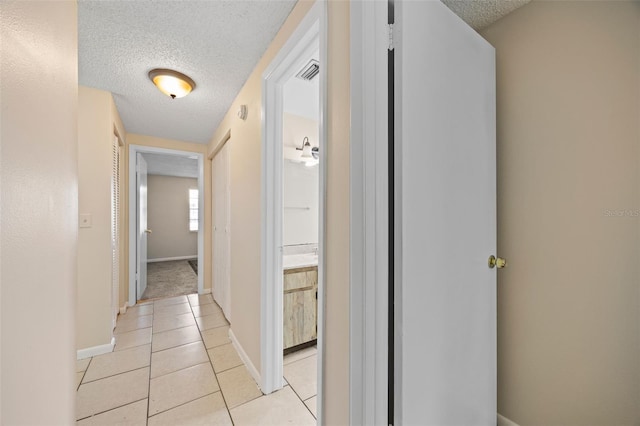 hall with visible vents, baseboards, a textured ceiling, and light tile patterned flooring