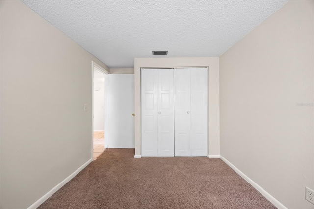 unfurnished bedroom featuring visible vents, a textured ceiling, a closet, carpet floors, and baseboards