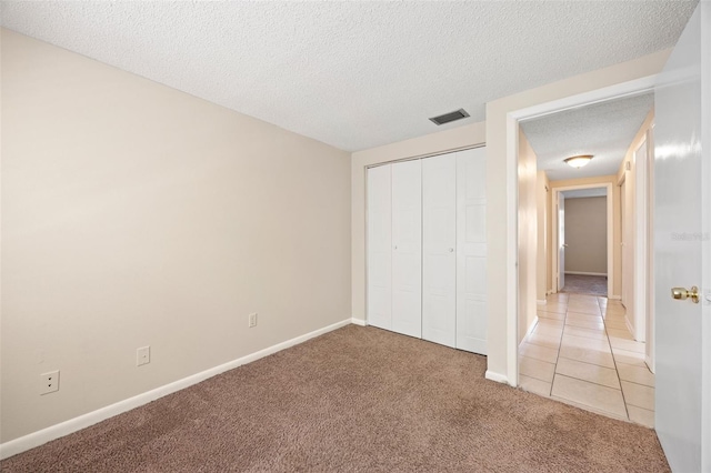 unfurnished bedroom featuring visible vents, baseboards, light carpet, a closet, and a textured ceiling