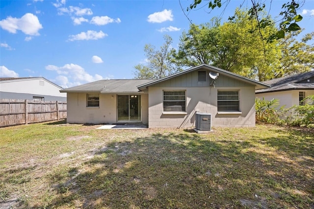 rear view of property with central AC unit, concrete block siding, a yard, and fence