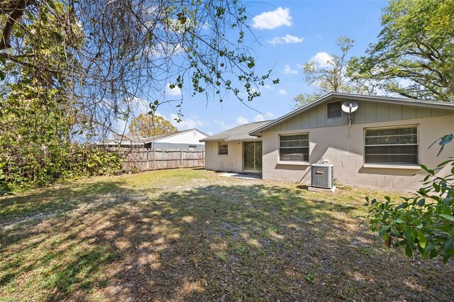 back of house featuring concrete block siding, a yard, fence, and cooling unit