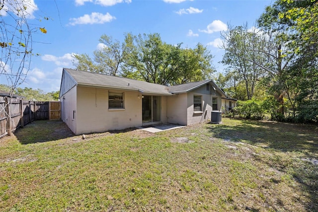 rear view of property with central air condition unit, a lawn, concrete block siding, and a fenced backyard