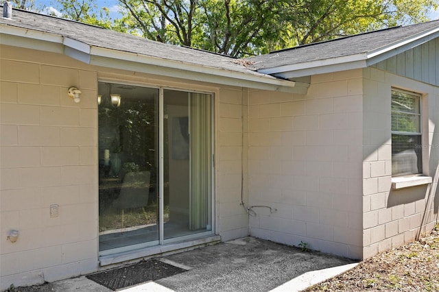 entrance to property with concrete block siding and a shingled roof