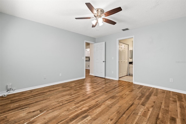 unfurnished bedroom with light wood-type flooring, visible vents, a textured ceiling, ensuite bath, and baseboards