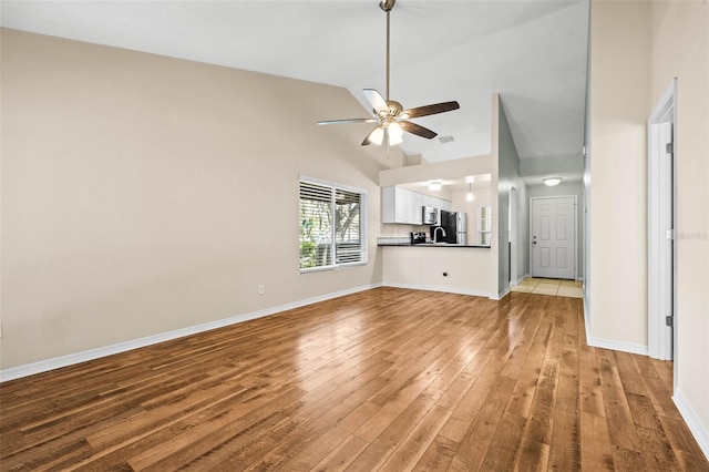 unfurnished living room with baseboards, high vaulted ceiling, a ceiling fan, and light wood finished floors