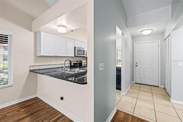 kitchen featuring a sink, dark countertops, appliances with stainless steel finishes, white cabinets, and baseboards