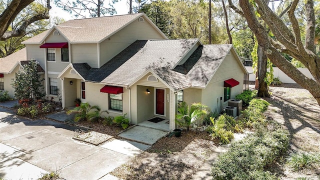 view of front facade with cooling unit, roof with shingles, and stucco siding