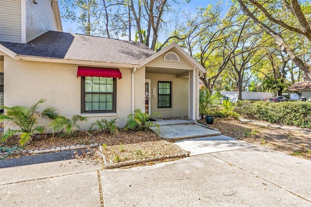 view of exterior entry featuring stucco siding and a shingled roof