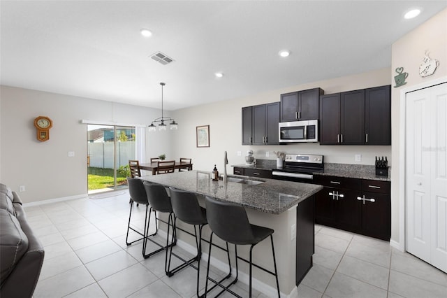 kitchen with visible vents, a sink, dark stone countertops, a kitchen breakfast bar, and stainless steel appliances