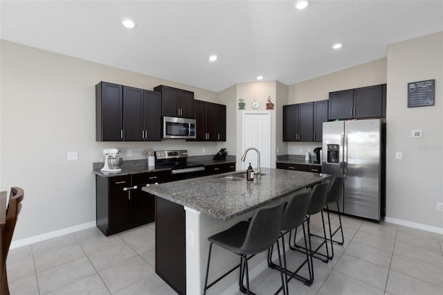 kitchen with a center island with sink, a sink, dark stone countertops, stainless steel appliances, and a breakfast bar area