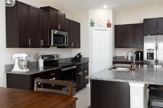 kitchen featuring dark stone countertops, light tile patterned floors, a sink, stainless steel appliances, and dark brown cabinets