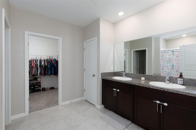 bathroom featuring a sink, a walk in closet, baseboards, and double vanity