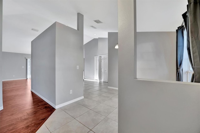 hall featuring light tile patterned floors, visible vents, baseboards, and high vaulted ceiling