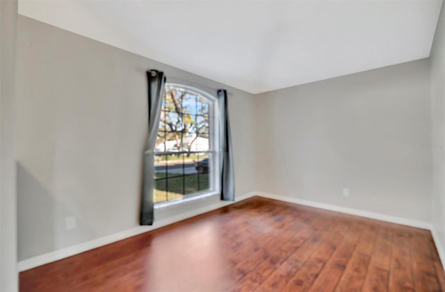 spare room with baseboards and wood finished floors