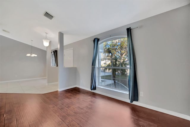 empty room with wood finished floors, visible vents, baseboards, lofted ceiling, and a notable chandelier