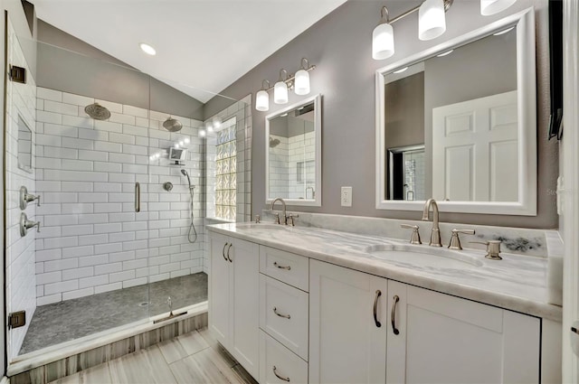 bathroom featuring vaulted ceiling, double vanity, a stall shower, and a sink