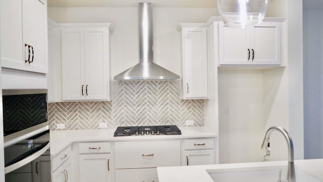 kitchen featuring stainless steel gas cooktop, a sink, light countertops, white cabinets, and wall chimney exhaust hood