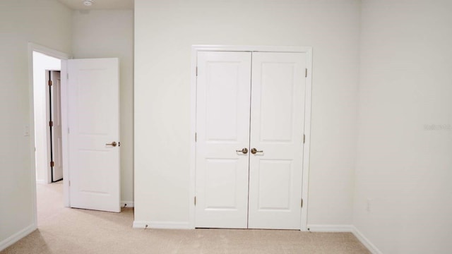 unfurnished bedroom with baseboards, a closet, and light carpet