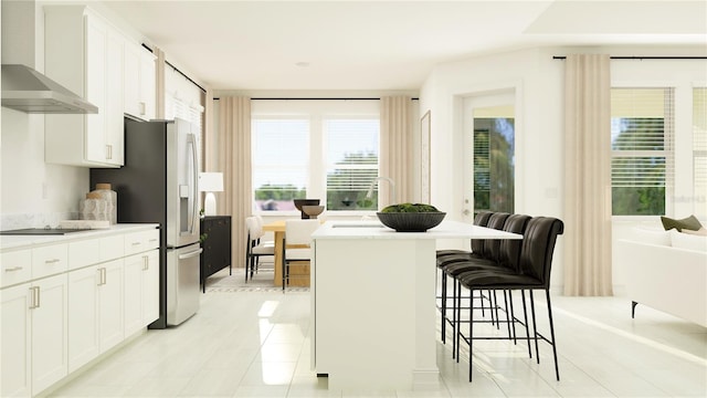 kitchen featuring stainless steel refrigerator with ice dispenser, a kitchen breakfast bar, wall chimney exhaust hood, white cabinets, and light countertops