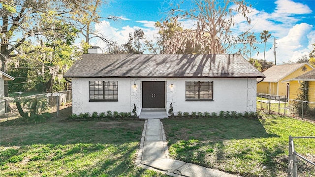 view of front facade with a shingled roof, a front lawn, fence, and stucco siding