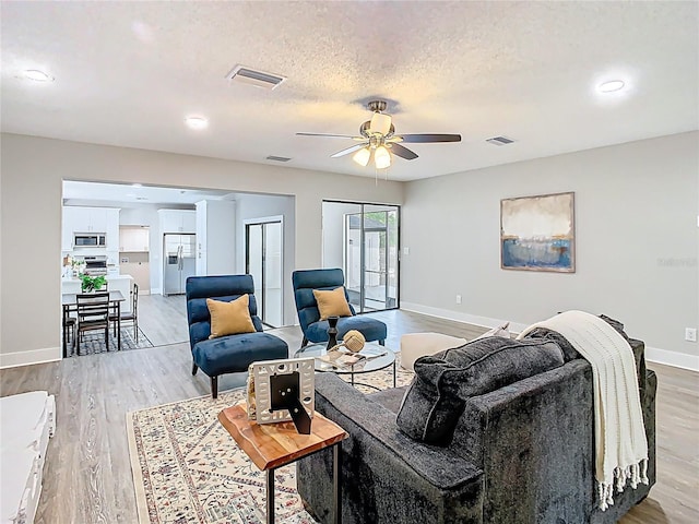 living room featuring visible vents, light wood finished floors, and a textured ceiling