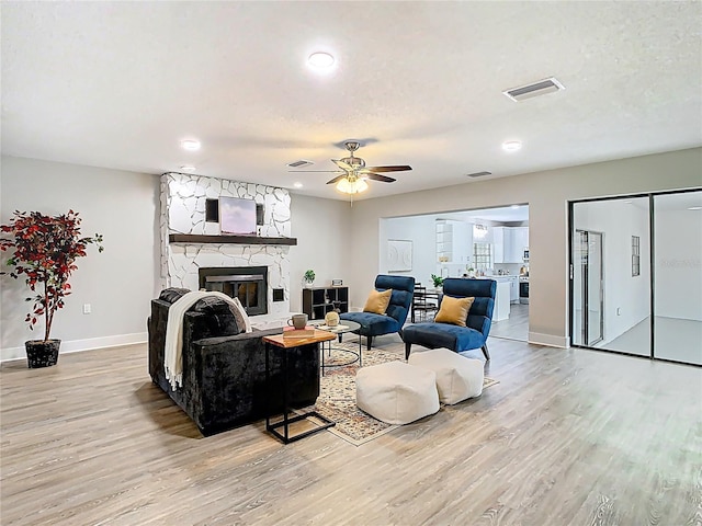 living room featuring visible vents, baseboards, light wood-style flooring, a fireplace, and a ceiling fan