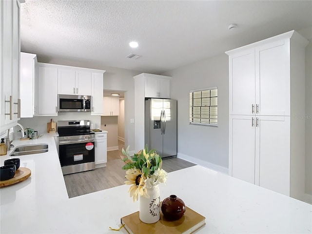 kitchen with visible vents, a sink, stainless steel appliances, light countertops, and white cabinets