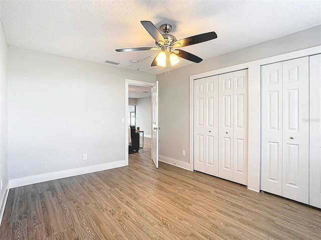 unfurnished bedroom featuring visible vents, two closets, light wood-type flooring, and baseboards