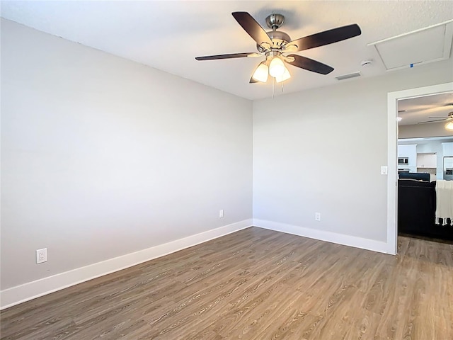 spare room featuring visible vents, baseboards, ceiling fan, attic access, and wood finished floors