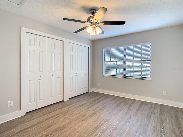 unfurnished bedroom with baseboards, two closets, wood finished floors, and a textured ceiling