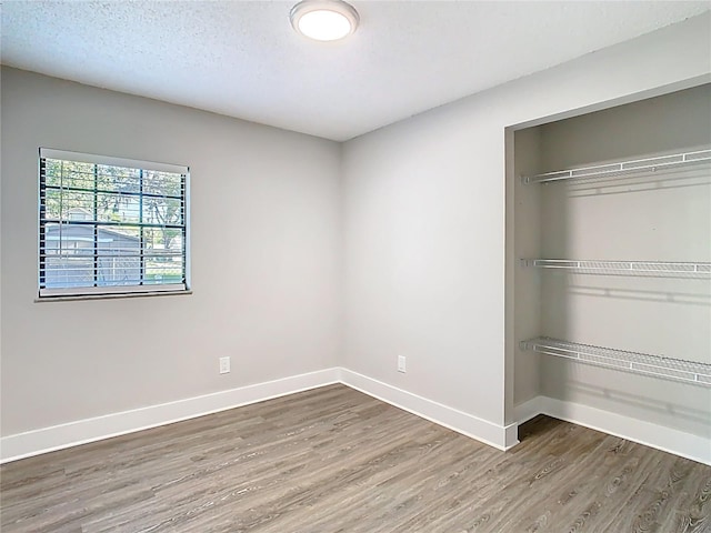 unfurnished bedroom featuring a closet, baseboards, a textured ceiling, and wood finished floors