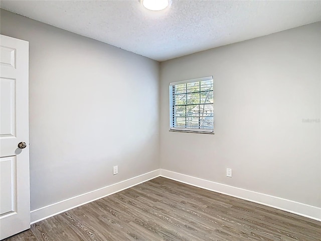 empty room with baseboards, a textured ceiling, and wood finished floors