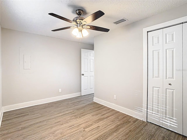 unfurnished bedroom featuring wood finished floors, baseboards, visible vents, a closet, and a textured ceiling