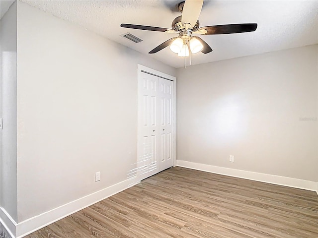 unfurnished bedroom with visible vents, a textured ceiling, wood finished floors, a closet, and baseboards