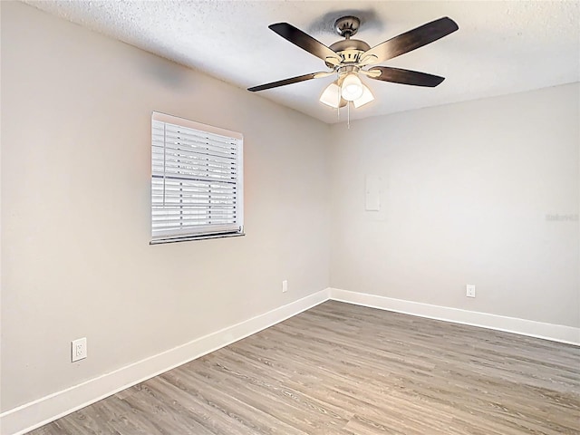 empty room with a ceiling fan, wood finished floors, baseboards, and a textured ceiling