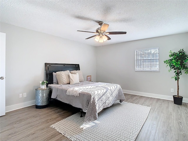 bedroom with a textured ceiling, a ceiling fan, baseboards, and wood finished floors