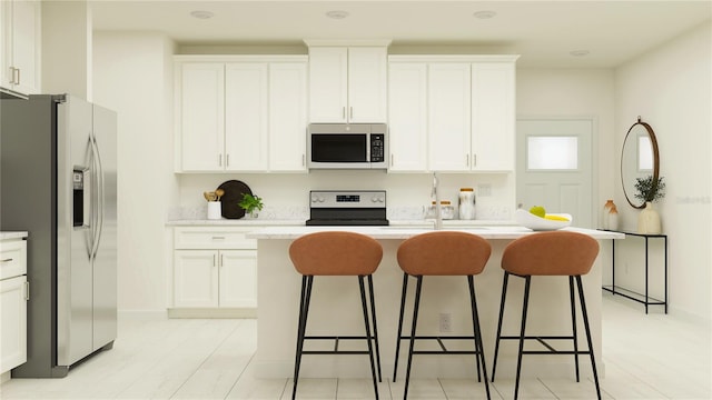 kitchen with a breakfast bar, an island with sink, a sink, white cabinetry, and appliances with stainless steel finishes